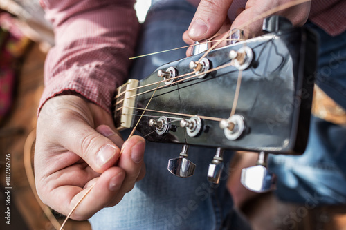 man pulls new guitar strings acoustic guitar in closeup