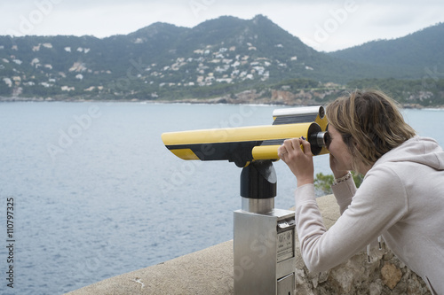 Young woman looking through coin-operated tourist telescope