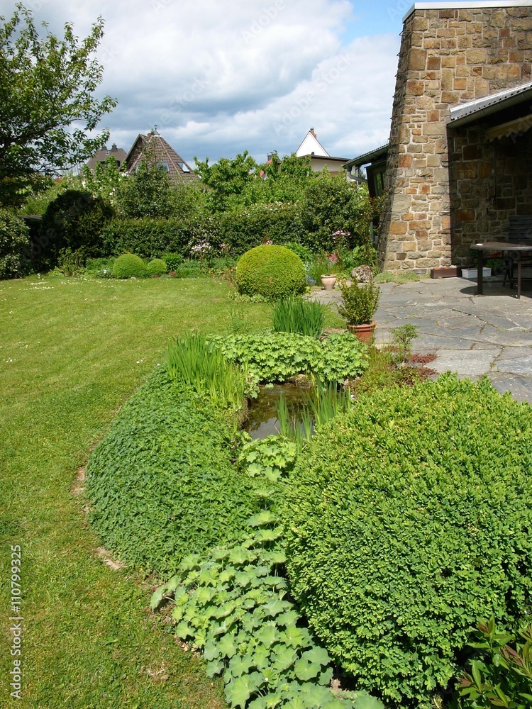Terrasse mit Kaminmauer aus Naturstein und schön angelegtem grünen