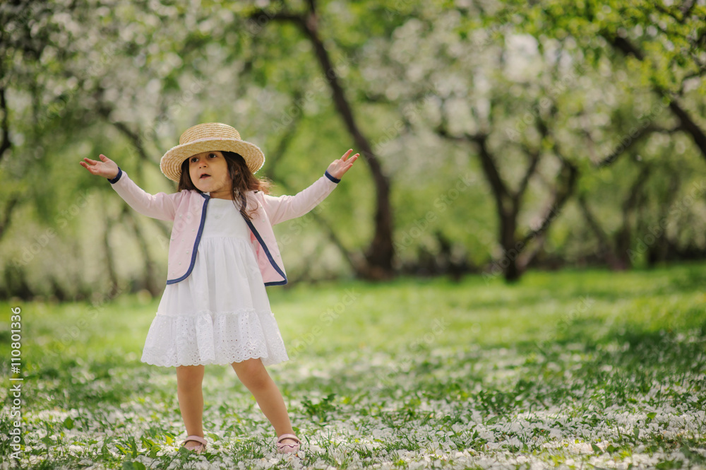 cute smiling dressy baby girl on the walk in blooming cherry garden in spring. Cozy rural scene, happy childhood concept