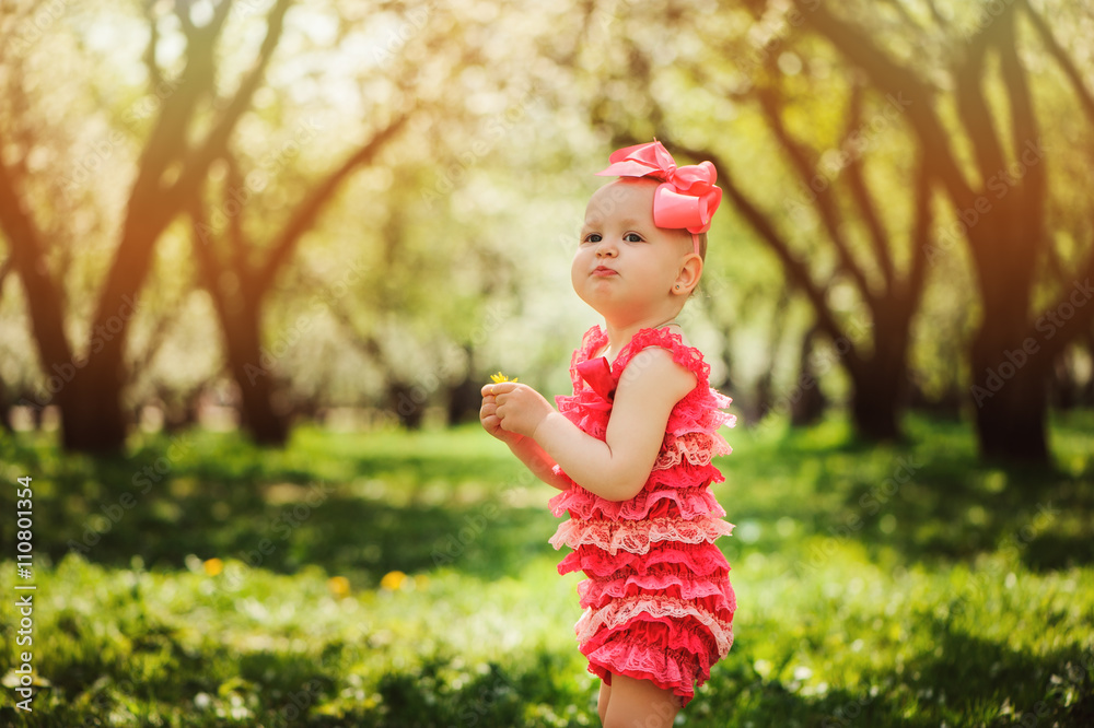 cute happy baby girl in funny pink romper walking outdoor in spring garden. Happy childhood concept cute happy baby girl in funny pink romper walking outdoor in spring garden. Happy childhood concept
