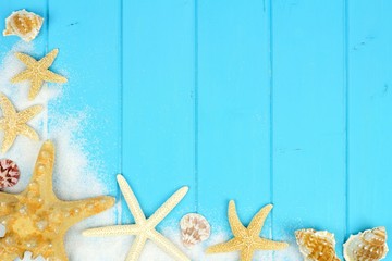 Summer corner border of sand, sea shells and star fish on blue wooden background