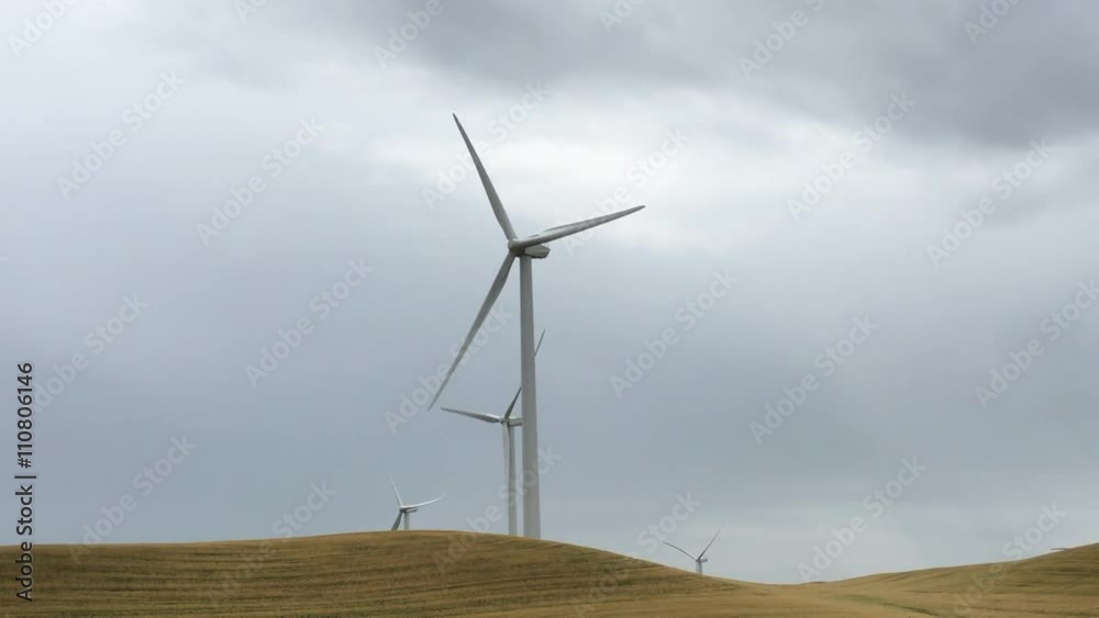 Windmills in a wheat field turning in the wind, storm clouds stormy sky in the background in Northern California Windmills in a wheat field turning in the wind, storm clouds stormy sky in the background in Northern California