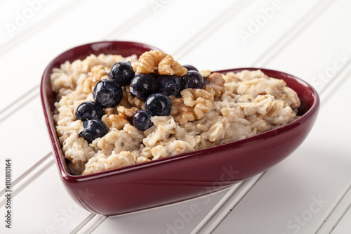 Heart shaped bowl with oatmeal, blueberries, and walnuts on white wood