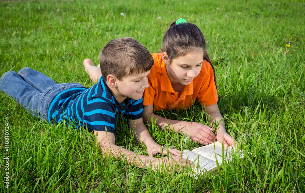 Fototapeta premium Two kids on green meadow with book