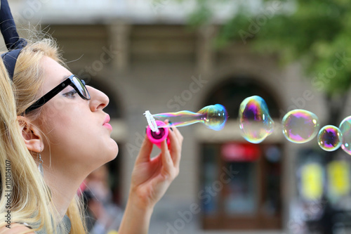 young woman with glasses blowing bubbles on street, side view