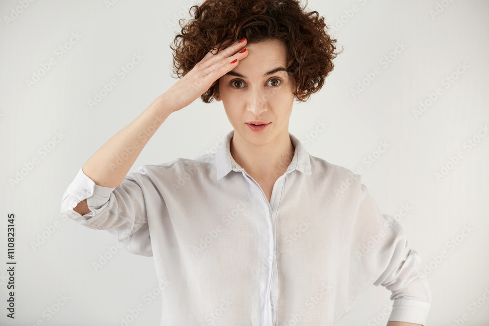 Human face expressions and emotions. Close up of young Caucasian female offiice worker in white shirt looking at the camera and holding head in astonisment while listening to some incredible story Human face expressions and emotions. Close up of young Caucasian female offiice worker in white shirt looking at the camera and holding head in astonisment while listening to some incredible story