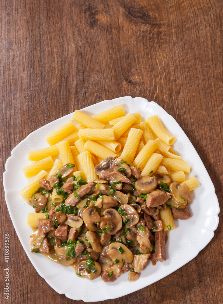 rigatoni pasta with meat and mushroom sauce in a plate on wooden table