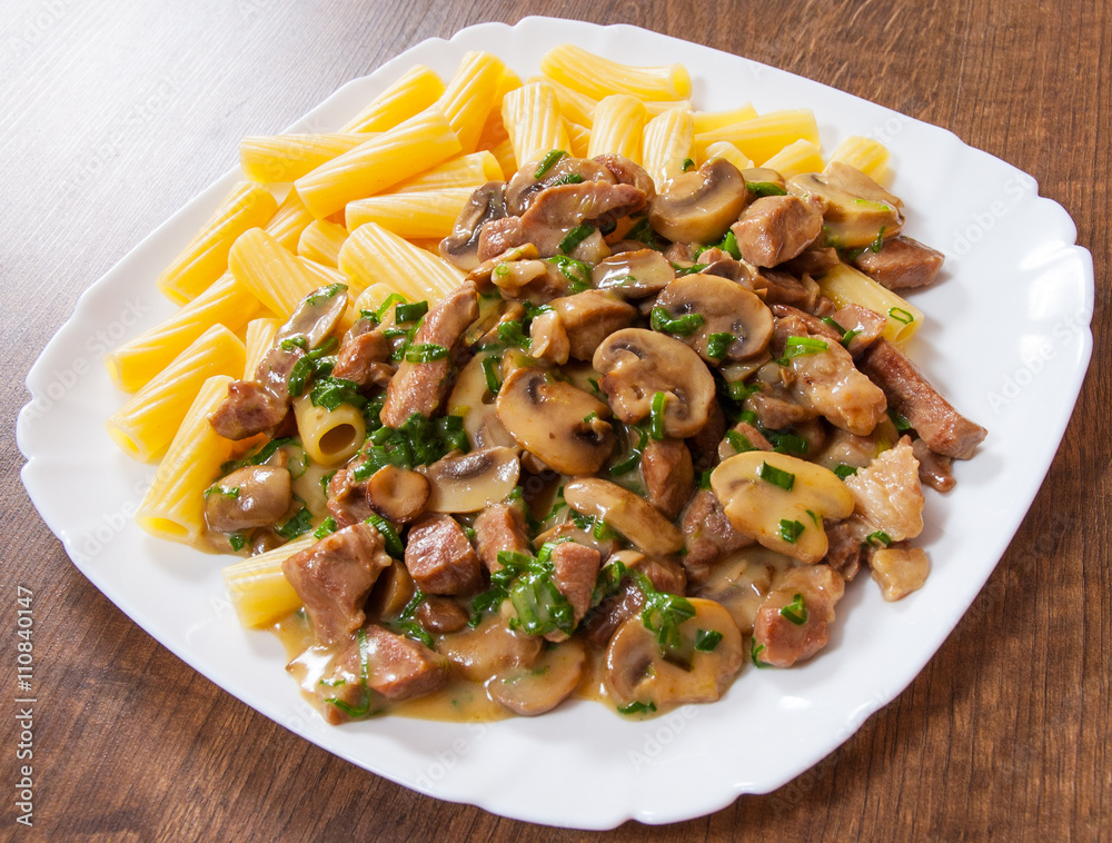 rigatoni pasta with meat and mushroom sauce in a plate on wooden table