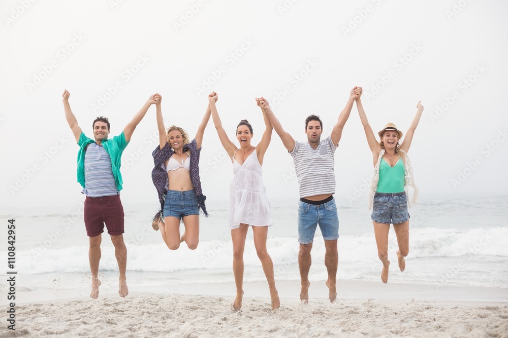 Obraz premium Portrait of friends holding hands and jumping on the beach
