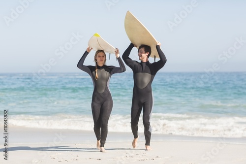 Happy couple in wetsuit carrying surfboard over the head photo