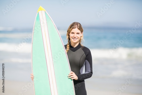 Portrait of woman in wetsuit holding a surfboard on the beach