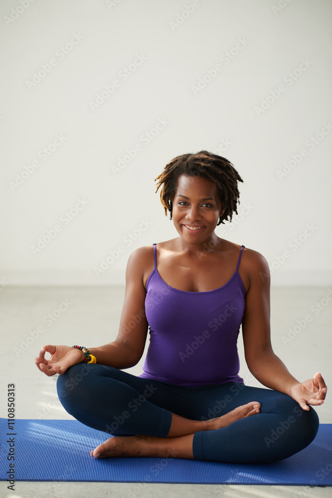 Smiling African-American woman sitting on yoga mat in lotus position
