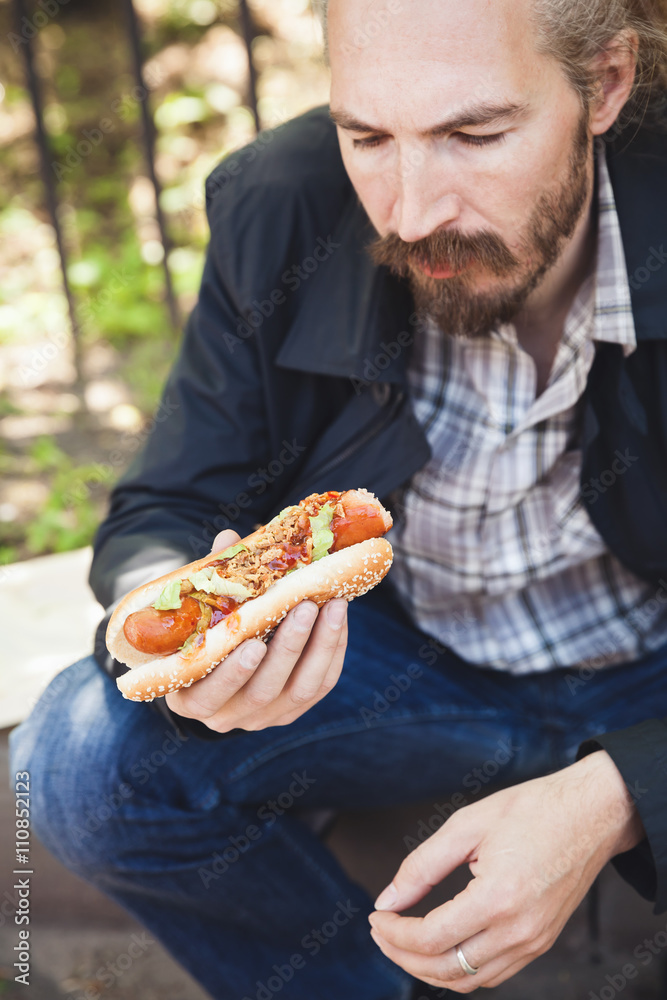 Bearded Asian man eating hot dog in summer