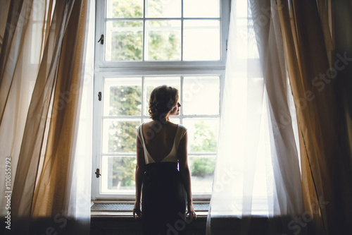 frail lady standing near a large window