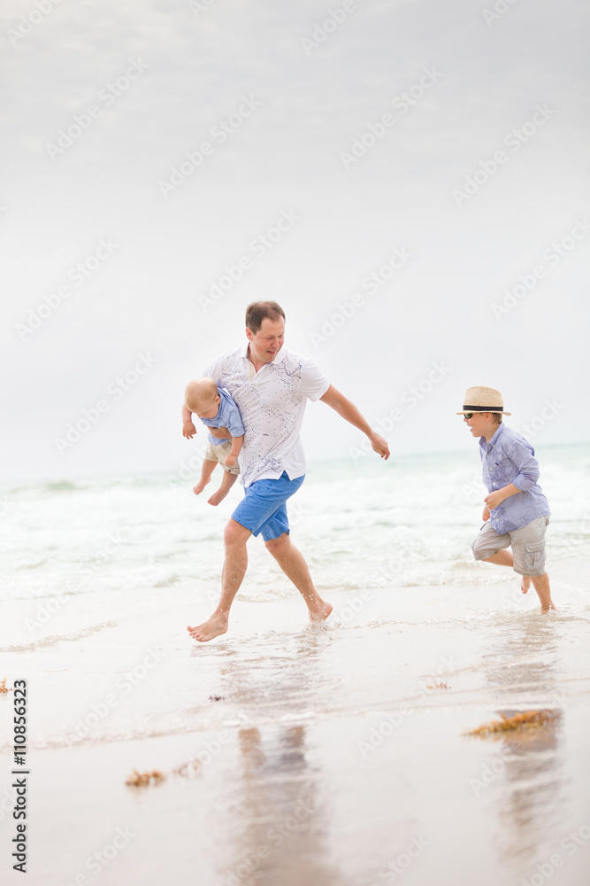 Portrait of father with two sons walking on the ocean beach. Summer vacations by the sea. Outdoors. Happy family.