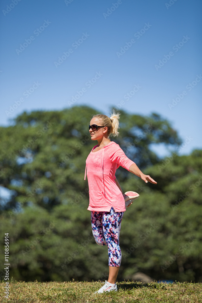 Young sportive woman stretching in the sunny park, outdoors. Working out outside. Healthy lifestyle. Doing exercises. Blue sky background. Young sportive woman stretching in the sunny park, outdoors. Working out outside. Healthy lifestyle. Doing exercises. Blue sky background.