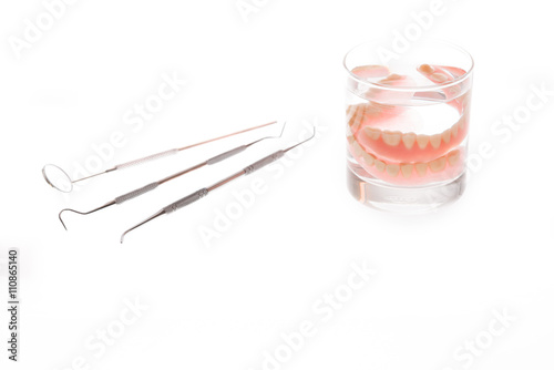 dentures in glass of water and tools on white background