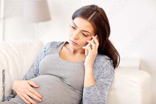 sad pregnant woman calling on smartphone at home