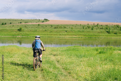 Man with a backpack going by bike along the river Dnister in Ukraine © iradzvonkovska