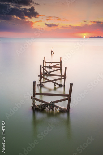 The view of an old, unused wooden pier on calm sea during cloudy sunset