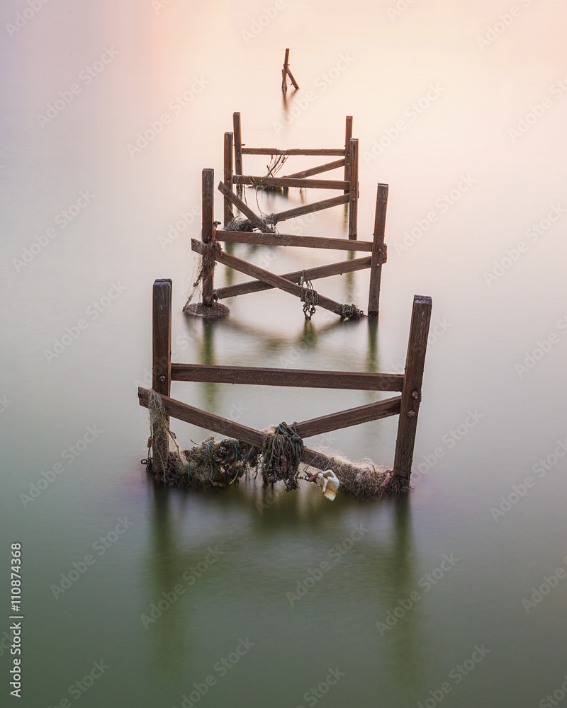 Obraz premium An old, unused wooden fishing pier on very calm sea during dusk.