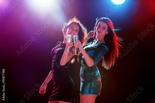 Two beautiful girls dancing at the party drinking champagne