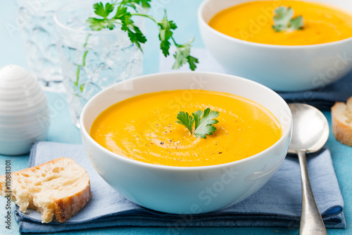 Pumpkin and carrot soup with cream and parsley on blue stone background.