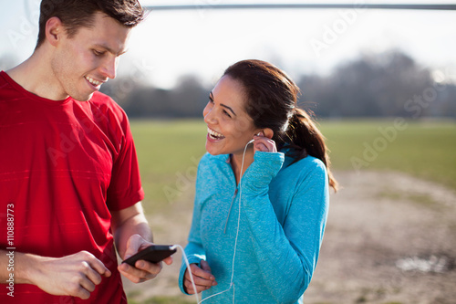 Young woman and man training, selecting smartphone music on playing field photo