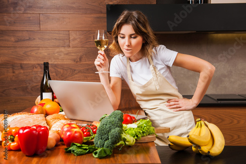 Canvas Print Pretty housewife reading from her laptop and drinking wine