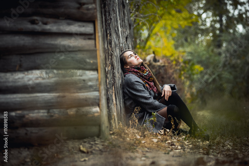 Beautiful young girl sitting at a wooden fence in the autumn