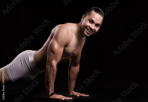 Young muscular man doing push-ups on black background.