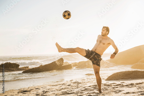 Mid adult man playing soccer keepy uppy on beach, Cape Town, South Africa photo
