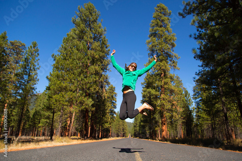 Young woman jumping mid air on forest road, Sisters, Oregon, USA photo