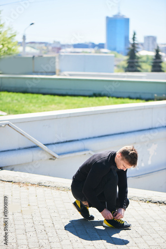 The athlete straightens his sneakers against the background of the city