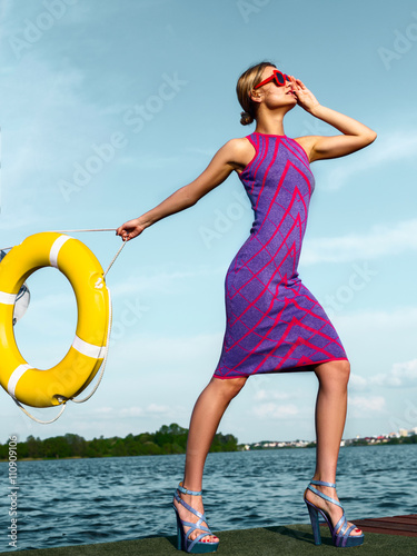 Beautiful girl in a purple dress and red sunglasses on the dock