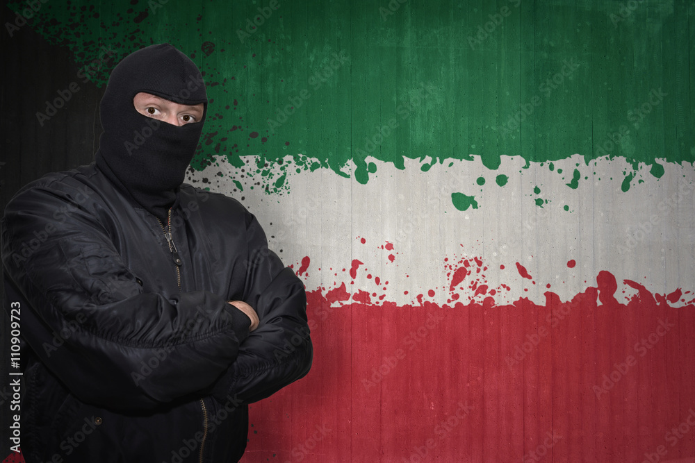 dangerous man in a mask standing near a wall with painted national flag of kuwait