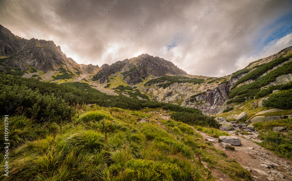 Mountain Landscape with Skok Waterfall under Dramatic Glowing Sky and Sun Shining From Behind the Peaks. Mlynicka Valley, High Tatra, Slovakia.
