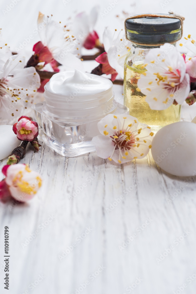 Face cream, fragnat oil and decorative stone with blossom on rustic wooden background