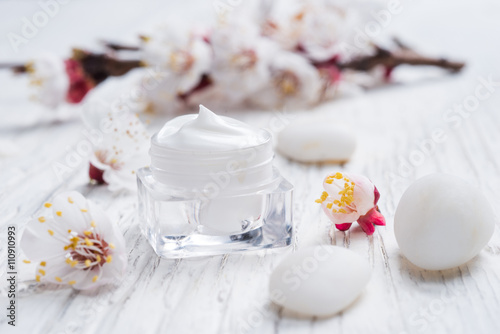 Facial cream with beauty cherry blossoms and white pebblestone on wooden background