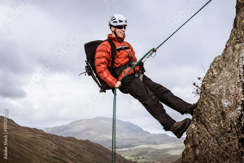 Young male climber abseiling down rock, The Lake District, Cumbria, UK
