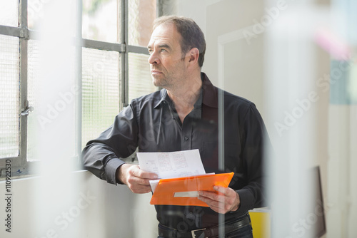 Businessman reading paperwork and gazing out of office window