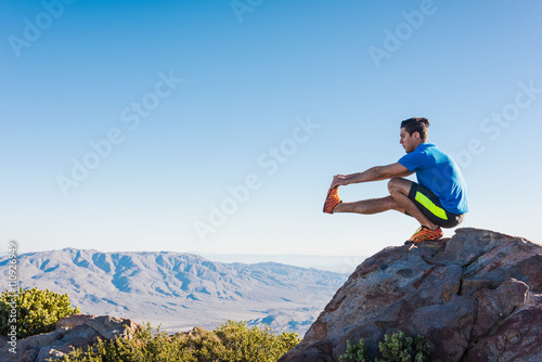 Male trail runner stretching legs on rock on Pacific Crest Trail, Pine Valley, California, USA photo