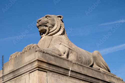 Laying lion statue on a pedestal against a blue sky 