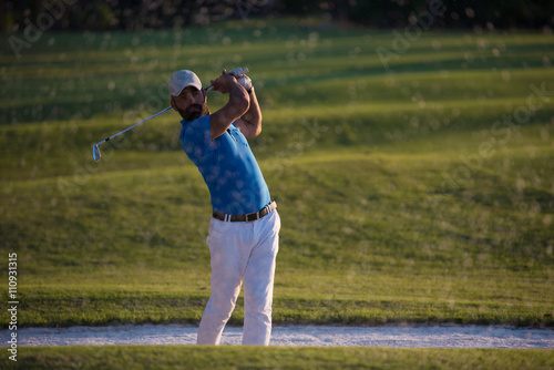 golfer hitting a sand bunker shot on sunset