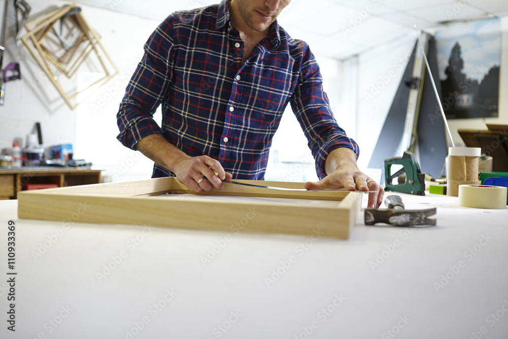 Mid adult man measuring frame on workbench in picture framers workshop Mid adult man measuring frame on workbench in picture framers workshop