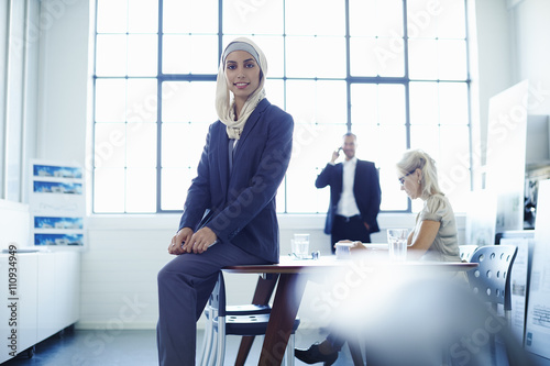 Portrait of young businesswoman sitting on office desk photo