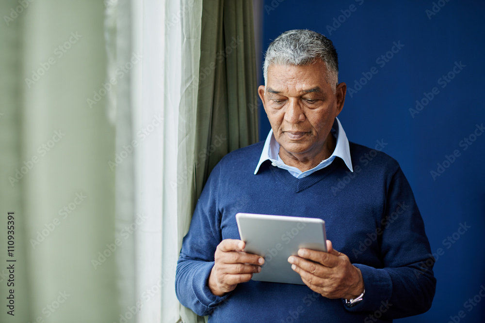 Pensive old man with digital tablet standing at window Pensive old man with digital tablet standing at window