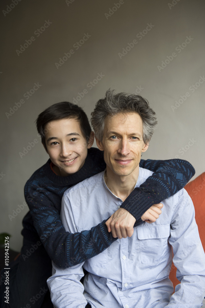 Portrait of teenage boy with arms around father on sofa Portrait of teenage boy with arms around father on sofa