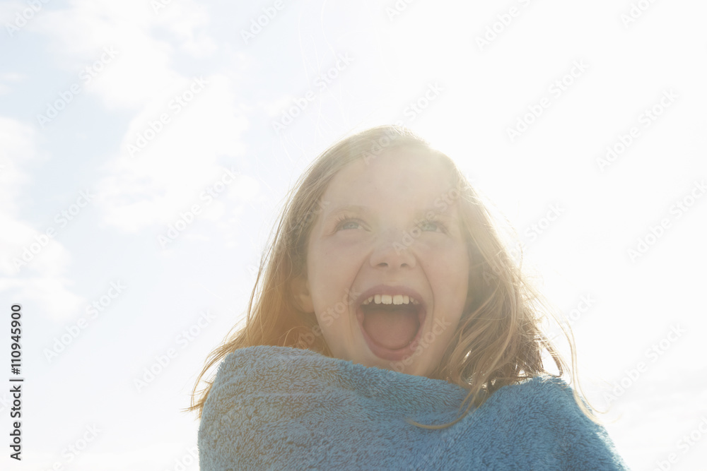 Portrait of laughing girl wrapped in towel at sunlit coast